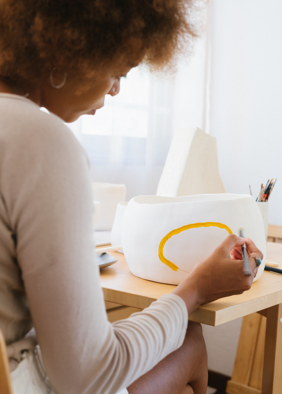 Focused African American ceramist painting pottery in workshop